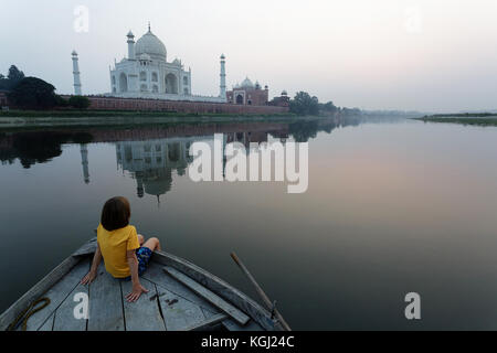 Jeune garçon assis sur un vieux bateau traditionnel et regardant le coucher du soleil sur le Taj Mahal, Agra, Inde. Banque D'Images