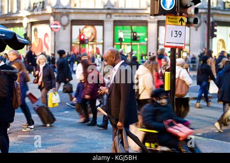 Man checking mobile phone alors que les acheteurs de noël lui passe inaperçu, Oxford circus, Londres, Royaume-Uni, 2017 Banque D'Images