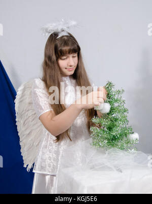 Une jeune fille dans un costume décore un petit sapin avec des pommes faites de coton Banque D'Images