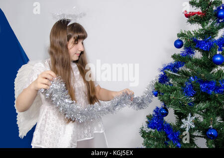 Une jeune fille dans un costume décore un arbre de Noël avec une tresse Banque D'Images