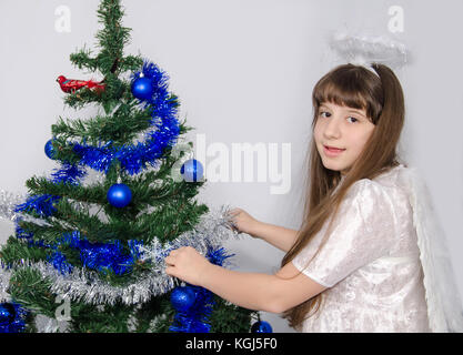 Une jeune fille dans un costume décore un arbre de Noël avec une tresse Banque D'Images