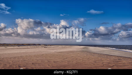 Plage de sable déserte avec douces vagues brisant le long du rivage sous un ciel nuageux ciel bleu cadre idyllique pour une escapade ou des vacances d'été Banque D'Images