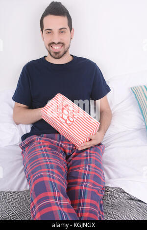 Young man eating popcorn et regarder des films détendu sur lit. à l'intérieur. Banque D'Images