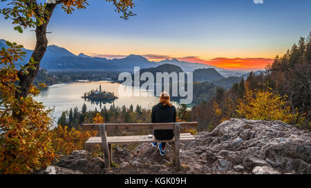 Bled, Slovénie - une femme coureur de cheveux rouge se détendant et profitant de la belle vue d'automne et du lever de soleil coloré du lac Bled assis sur une colline benc Banque D'Images