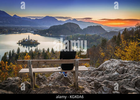 Bled, Slovénie - femme de coureur se détendant et profitant de la belle vue d'automne et du lever de soleil coloré du lac Bled assis sur un banc au sommet d'une colline portant Banque D'Images