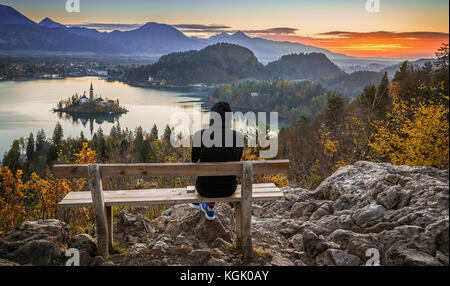 Bled, Slovénie - femme de coureur se détendant et profitant de la belle vue d'automne et du lever de soleil coloré du lac Bled assis sur un banc au sommet d'une colline portant Banque D'Images