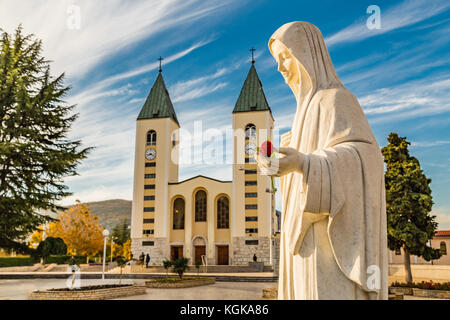 Statue de la Vierge Marie tenant une rose rouge alors que l'église Saint Jacques de Medjugorje est en arrière-plan Banque D'Images