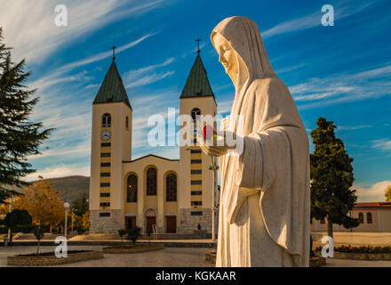 Statue de la Vierge Marie tenant une rose rouge alors que l'église Saint Jacques de Medjugorje est en arrière-plan Banque D'Images