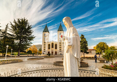 Statue de la Vierge Marie tenant une rose rouge alors que l'église Saint Jacques de Medjugorje est en arrière-plan Banque D'Images