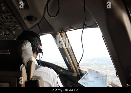 Assis sur un pilote en strapontin d'envol avec casque, communiquer avec tour, regardant à travers une fenêtre de l'avion, juste avant l'atterrissage Banque D'Images