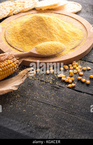 Avec une pile verticale de l'image de la farine de maïs sur une planche en bois, un épi de maïs et les grains de maïs soufflé, des gâteaux dans l'arrière-plan, sur une table en bois rustique. Banque D'Images