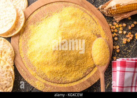 High angle view image avec un tas de farine de maïs sur une table ronde en bois, entourée d'épis de maïs, les grains de maïs soufflé et de gâteaux, sur une table en bois noir Banque D'Images