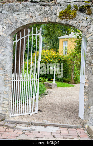 Porte de jardin en fer forgé blanc ouvrant sur un jardin avec des buissons verts et un tableau d'oiseaux en Irlande Offaly Banque D'Images