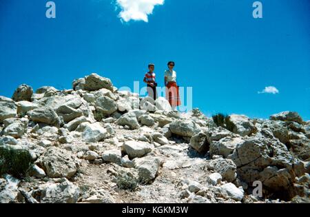 Une mère et son fils se tiennent debout au sommet d'un tas de rochers au parc national Crater dans le comté de Klamath, Oregon, tous deux portant des tenues rouge et blanche coordonnées, le fils portant un appareil photo, un jour ensoleillé, 1952. () Banque D'Images