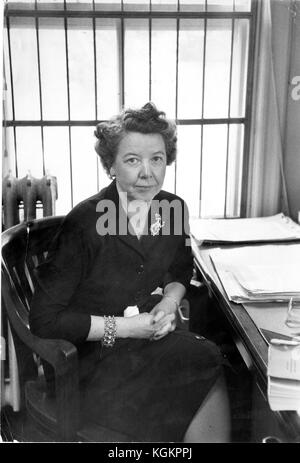 Portrait de Katharine Hafstad, historienne et chercheuse au Bureau de recherche opérationnelle de l'Université Johns Hopkins, assise au bureau portant une robe et une broche, les mains sur les genoux, devant un bureau avec des piles de papiers, environ 45 ans, Baltimore, Maryland, 1961. () Banque D'Images