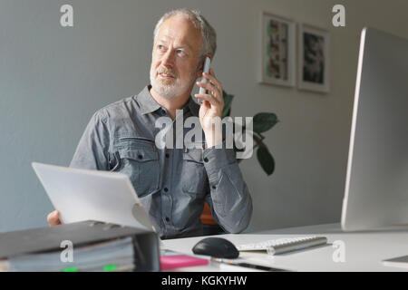 Mature businessman using mobile phone while sitting at desk in office Banque D'Images