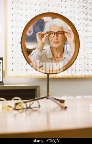 Portrait of senior woman wearing eyeglasses reflétant sur miroir par store Banque D'Images