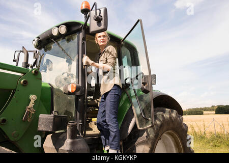 Low angle view of woman standing sur le tracteur à la ferme contre ciel lors de journée ensoleillée Banque D'Images