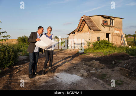 Femme debout avec agent immobilier lors de la lecture de documents contre chambre le jour ensoleillé Banque D'Images