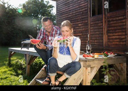 Mature couple enjoying watermelon slice en étant assis à l'extérieur ferme sur sunny day Banque D'Images