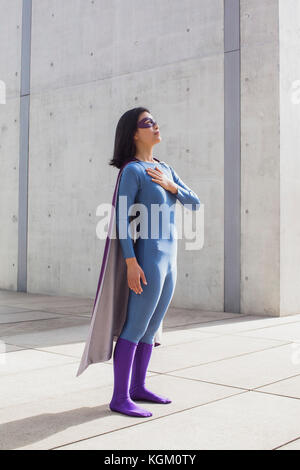 Woman wearing superhero costume debout sur marbre par wall Banque D'Images
