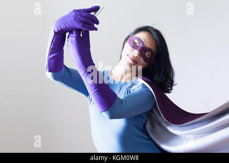 Jeune femme habillé en super héros en tenant contre selfies fond blanc Banque D'Images