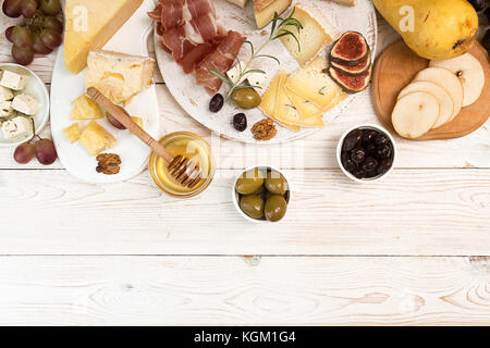 Frais d'assiette de fromage avec des morceaux de fromage moisi, le prosciutto, les prunes au vinaigre, olives, raisins, figues, miel, poire, noix sur fond de bois blanc. Haut Banque D'Images