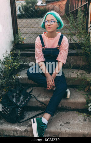 Longueur totale de teenage girl sitting on steps contre fence Banque D'Images