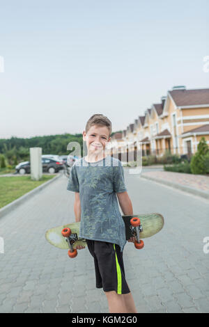 Portrait of smiling boy holding skateboard en se tenant sur le street contre ciel clair Banque D'Images