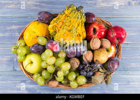 Panier tressé en bois plein de fruits d'automne comme les raisins, les pommes, les prunes, les noix et certaines citrouilles coloré. Banque D'Images