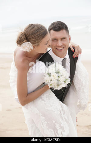 Groom donner piggyback ride à bride sur la plage Banque D'Images