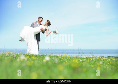 Groom holding bride d'armes en face de la mer Banque D'Images
