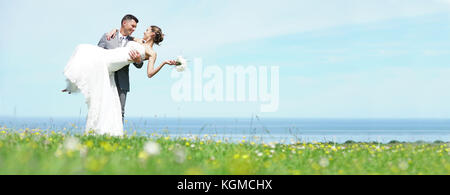 Groom holding bride d'armes en face de la mer Banque D'Images