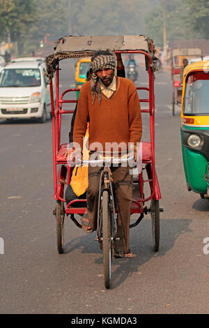 Delhi, Inde - le 20 novembre 2015 : cycle rickshaw rider transporte un passager dans le trafic encombré avec le smog visibles de la pollution atmosphérique Banque D'Images