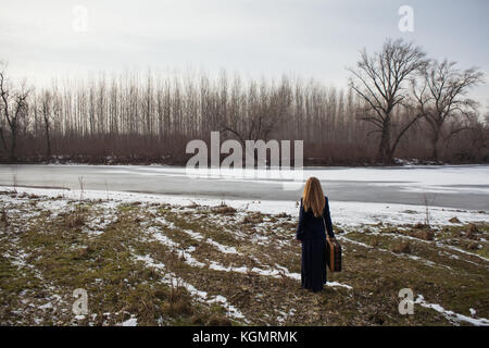 Femme debout près de rivière avec vieille valise et à la recherche d'un moyen d'aller Banque D'Images
