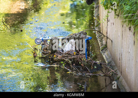 Chariot Tesco jeté jeté dans un ponceau couvert de mauvaises herbes et de déchets. Dans l'eau Banque D'Images