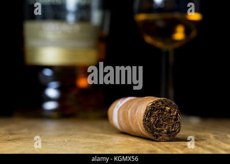 Photo en gros plan de la vie toujours avec un cigare, une bouteille d'alcool et un verre de whisky sur une vieille table en bois, avec un arrière-plan flou Banque D'Images