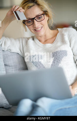 Femme d'âge moyen à la maison l'achat sur internet avec carte de crédit Banque D'Images