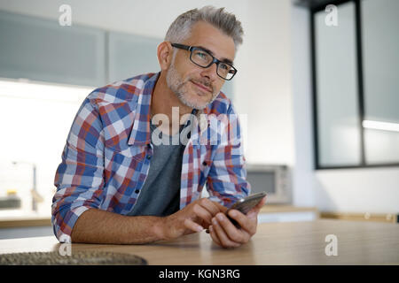 Homme d'âge moyen à la maison using smartphone Banque D'Images