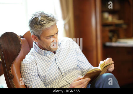 Man reading book en fauteuil à la maison Banque D'Images