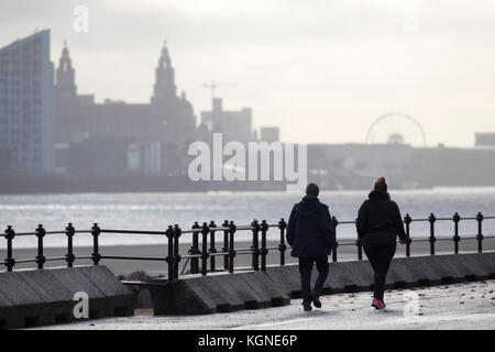 New Brighton wirral, uk weather. vent, averses passant au-dessus de l'ouest aujourd'hui pour laisser un bel après-midi, mais avec l'augmentation des vents. Un couple en prenant une marche matinale et robe pour les conditions plus froides un vent, le long de la promenade à new brighton avec la rivière Mersey et toits de Liverpool dans la distance Banque D'Images