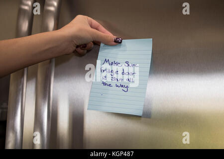 Young woman's hands en plaçant un post-it sur le réfrigérateur dans la cuisine Banque D'Images
