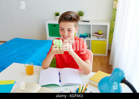 L'éducation, de la technologie et de la communication concept - happy student boy distraire de ses devoirs et texting on smartphone à la maison Banque D'Images