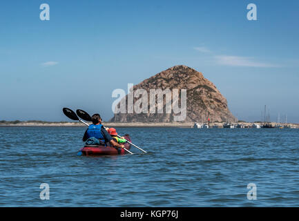 Un père et son fils, une pagaie kayak rouge tandem vers Morro Rock sur Morro Bay, le jeune garçon porte un chapeau orange, les deux sont ensemble pagaie Banque D'Images