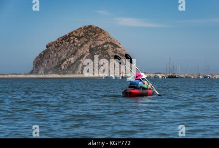 Deux jeunes filles une pagaie kayak rouge tandem vers Morro Rock in Morro Bay, Californie sur un matin ensoleillé. Banque D'Images