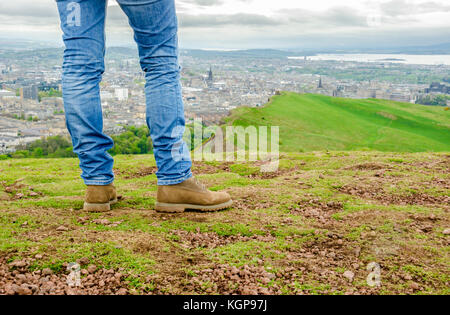 L'accent sur les jambes d'un modèle des femmes portant des jeans skinny et des bottes en daim marron admirant le paysage d'Édimbourg à partir du haut de l'Arthur's seat. scotla Banque D'Images