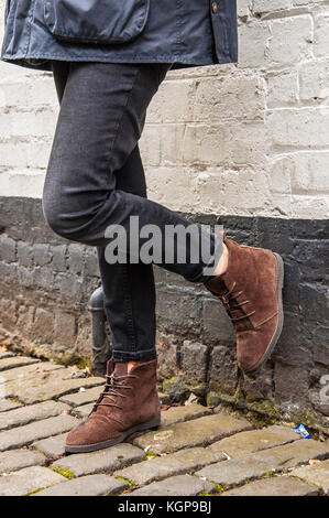 Les jambes du modèle portant un pantalon skinny noir serré et brown boots. noir et blanc mur en brique en un arrière-plan. Banque D'Images