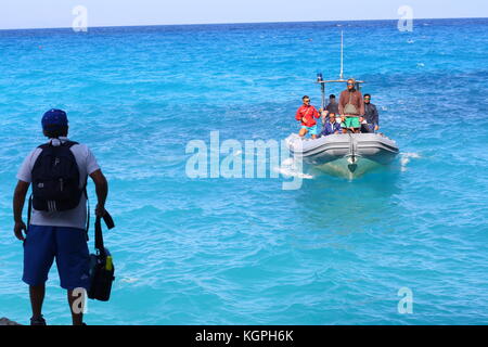 Un homme monte à bord d'un petit bateau gonflable Vigilanza sur l'eau de mer bleue dans un parc national sarde. Banque D'Images