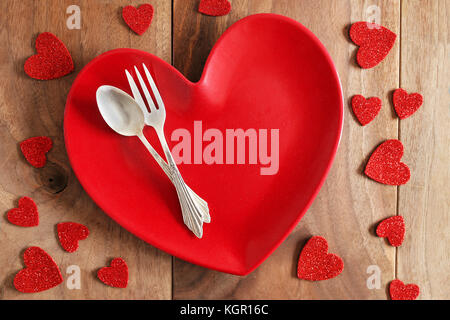 Un dîner en forme de coeur rouge, avec la plaque d'argent allemand fine fourchette et cuillère, est sur une table de planches en bois de cerisier rustique, entouré par la Saint-Valentin confe Banque D'Images