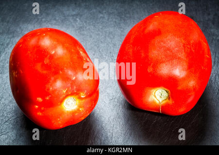 Tomates mûres (Solanum lycopersicum) sur une plaque en ardoise noire. Banque D'Images